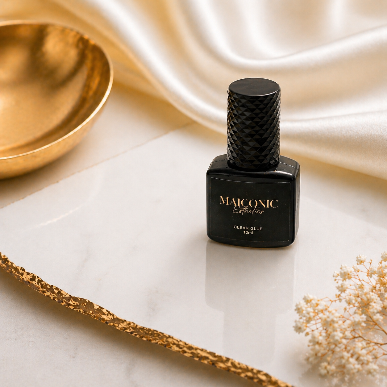 Black lash glue bottle with 'Maiconic Esthetics' branding on a marble surface with gold accents.
