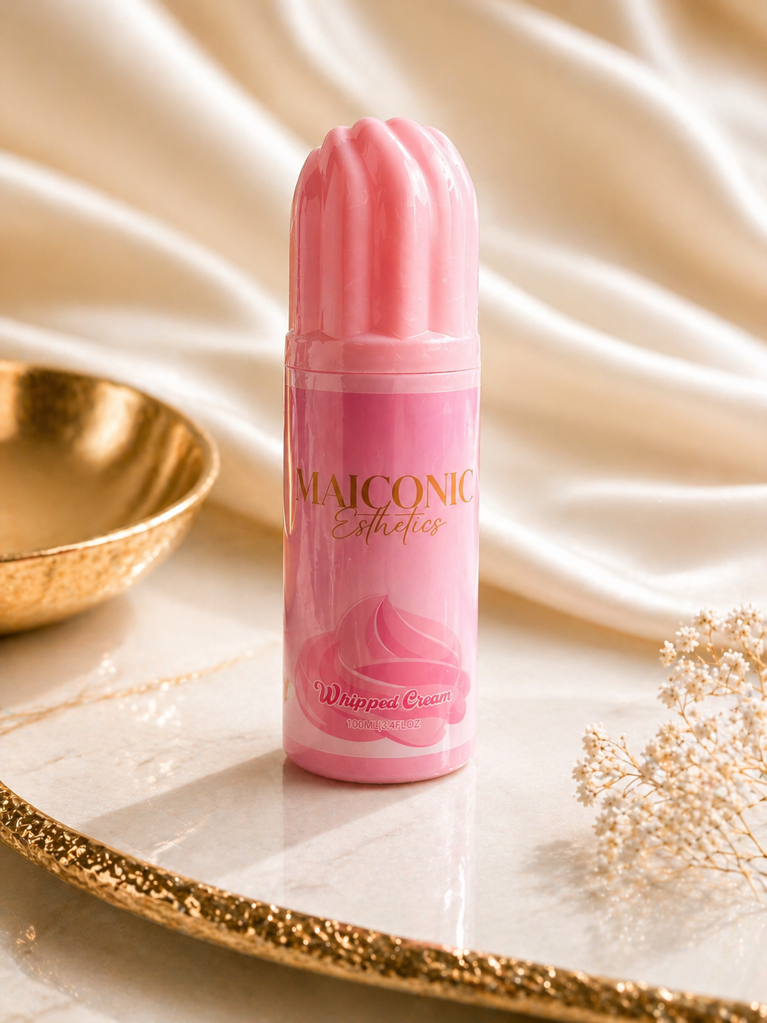 Pink whipped cream lash shampoo canister on a decorative surface with a gold bowl and white flowers.